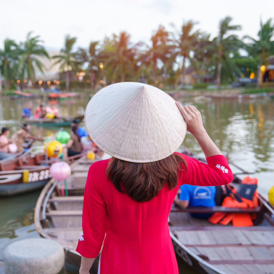 happy woman wearing Ao Dai Vietnamese dress, traveler visit Thu Bon River and Sightseeing Boat Ride at Hoi An ancient town. landmark for tourist attractions.Vietnam and Southeast travel concept